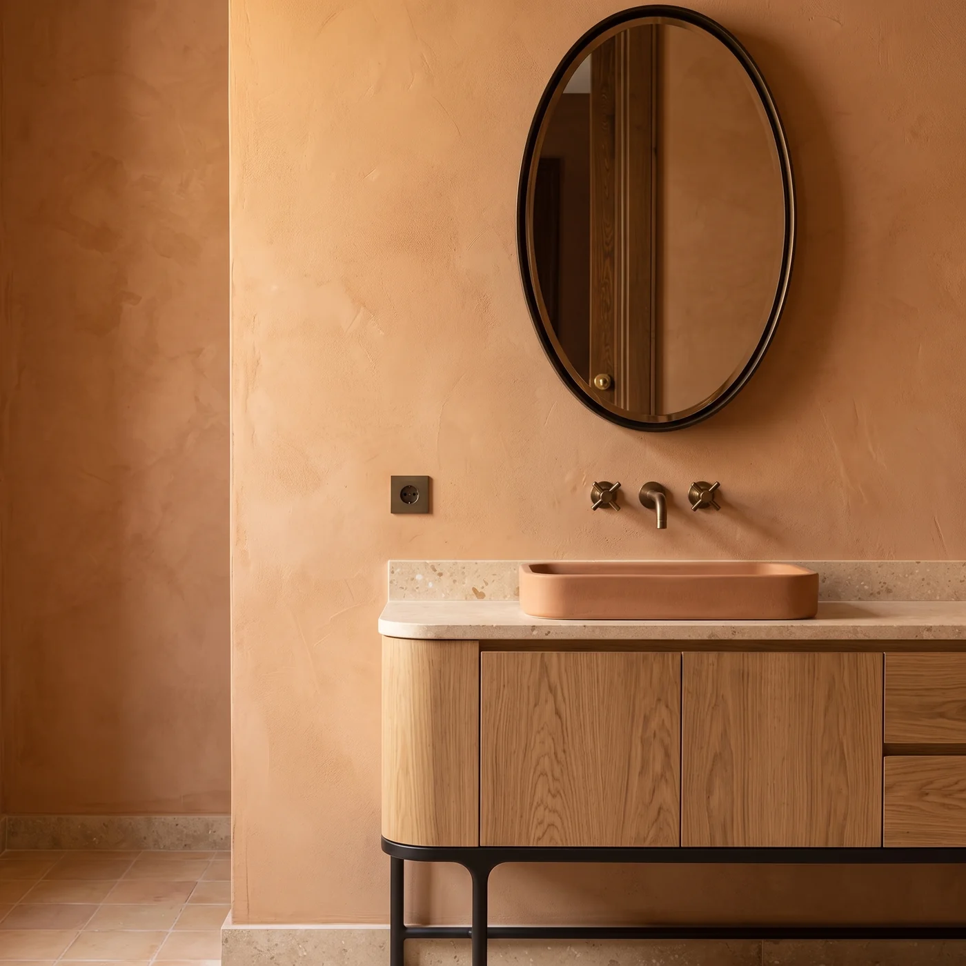 Vanité en chêne sous un miroir ovale, vasque rose argile et robinetterie en bronze sur un mur ocre